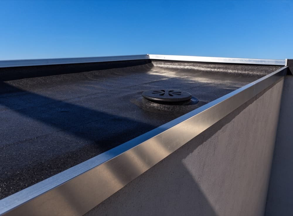 Afgewerkt plat dak met zwarte EPDM, aluminium daktrim en een ronde afvoer
