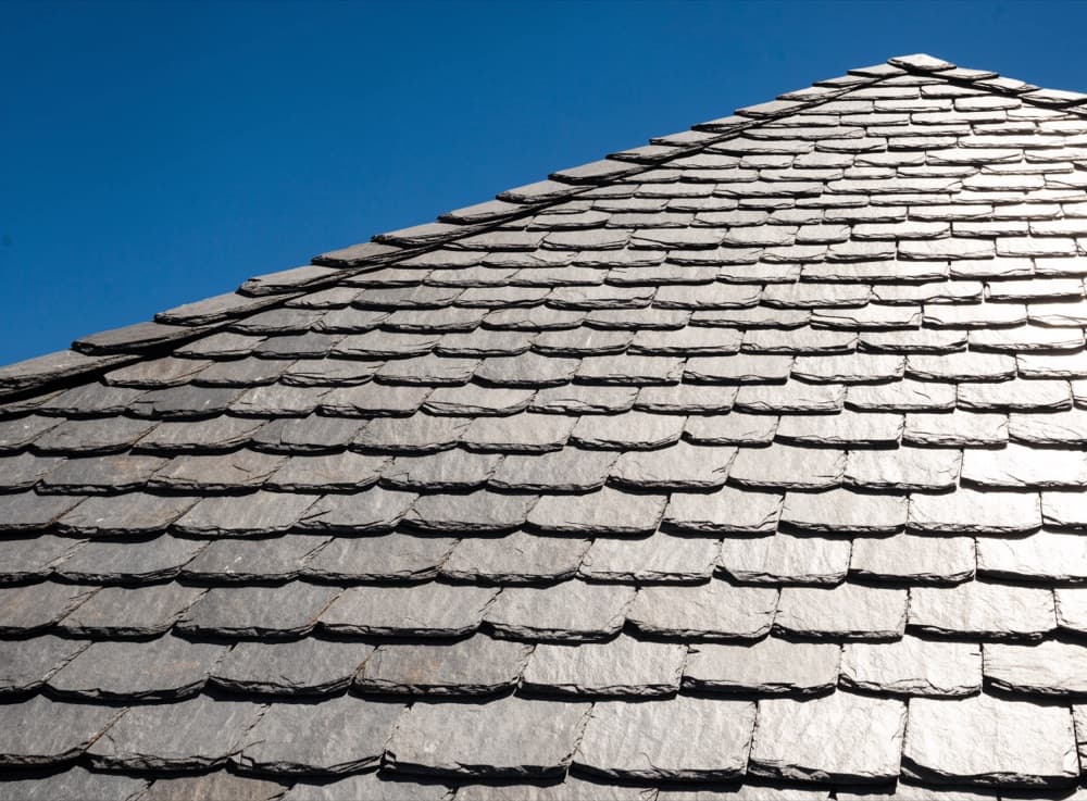 Grijze natuurleien in overlappende rijen op een steil dakvlak